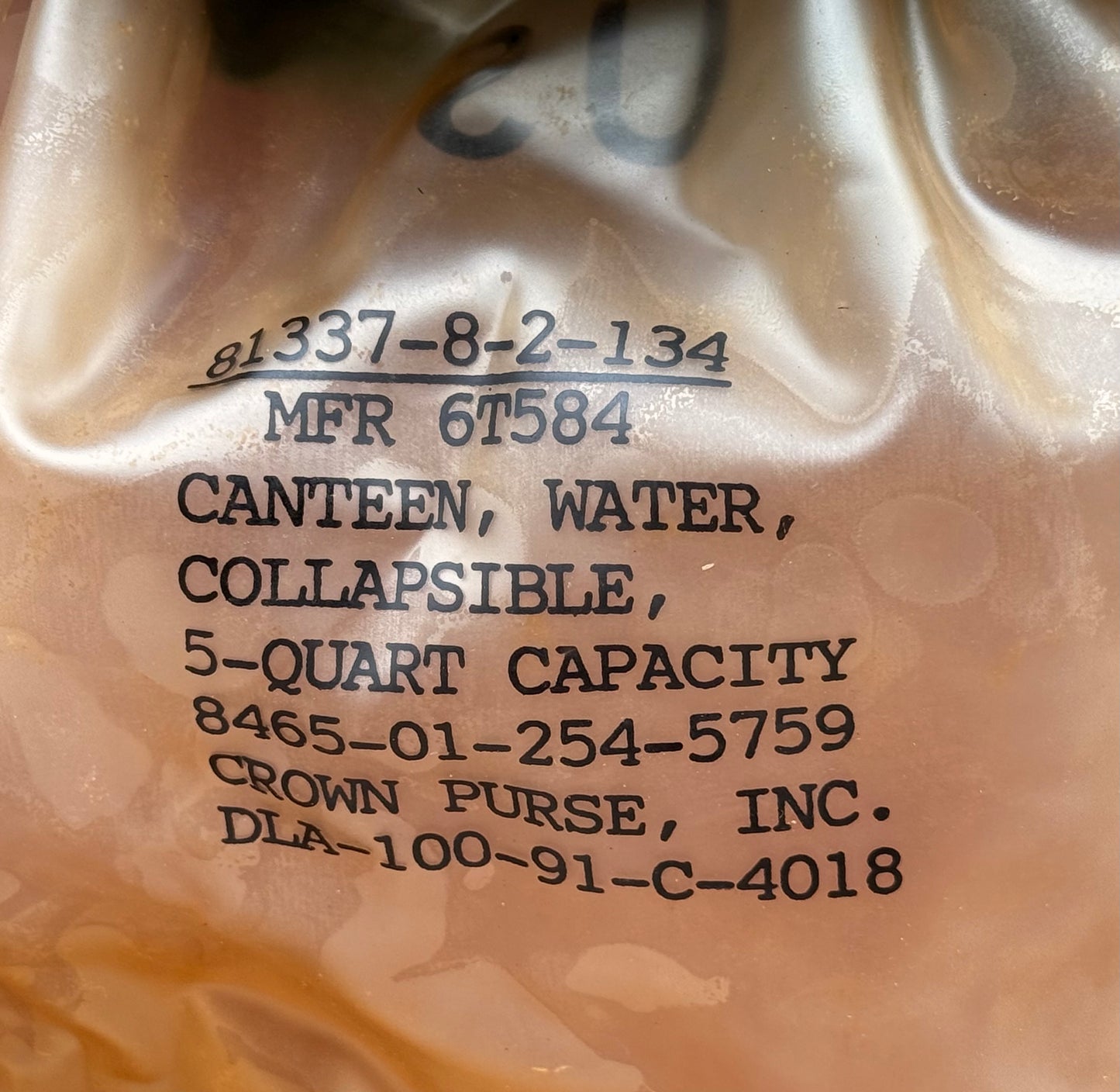 Close-up of a translucent beige plastic water canister with black printed text identifying it as a 5-quart collapsible water can by Crown Purse, Inc.