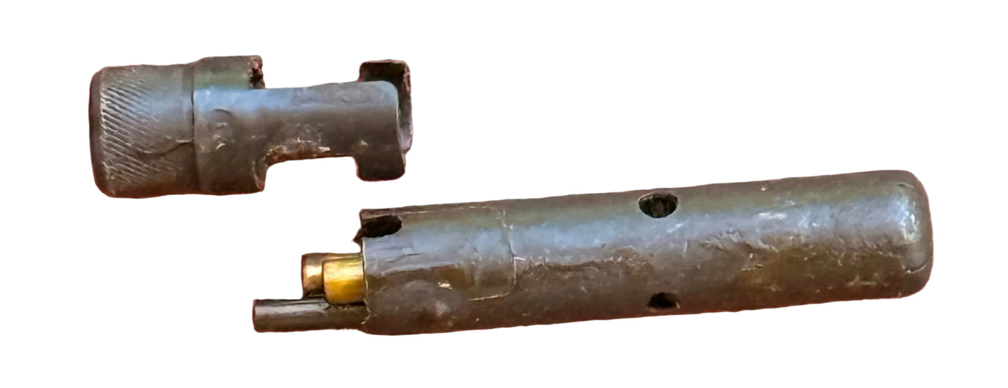 A close-up of a small cylindrical metal object with a threaded cap and a brass-toned inner piece, placed on a textured reddish-pink background.