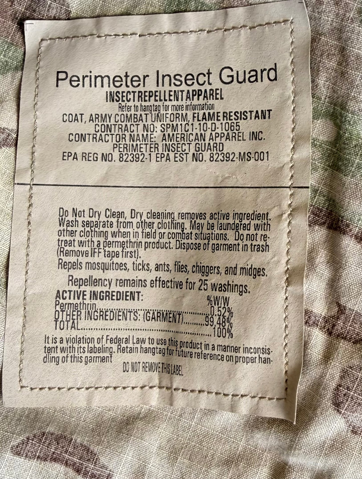 A close-up of a sewn fabric product label reading 'Perimeter Insect Guard' with product details and ingredients, placed on a textured beige and brown fabric background.