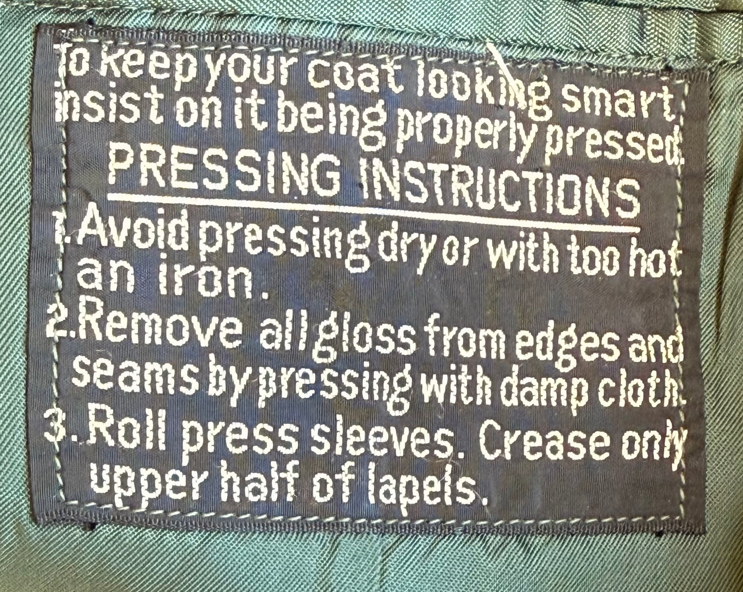 A close-up of a sewn fabric label with white text reading pressing instructions for a coat, including avoiding dry ironing and rolling press sleeves.