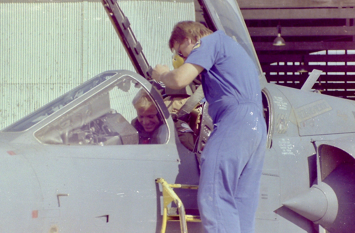 Person in blue jumpsuit interacting with a small aircraft inside a hanger.