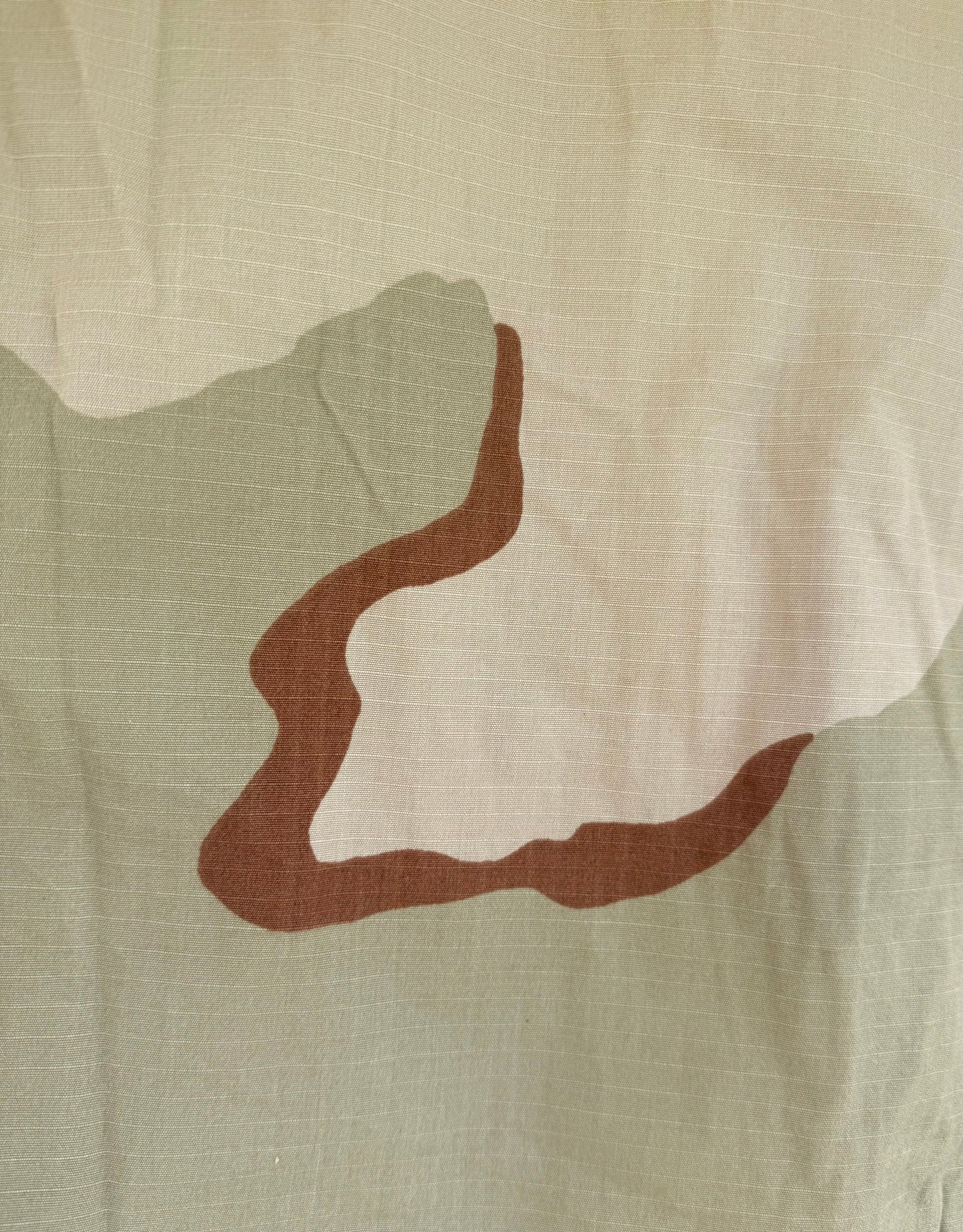 A close-up of a fabric surface with a large abstract organic shape in medium brown on an off-white base, with a muted sage green shape behind it.