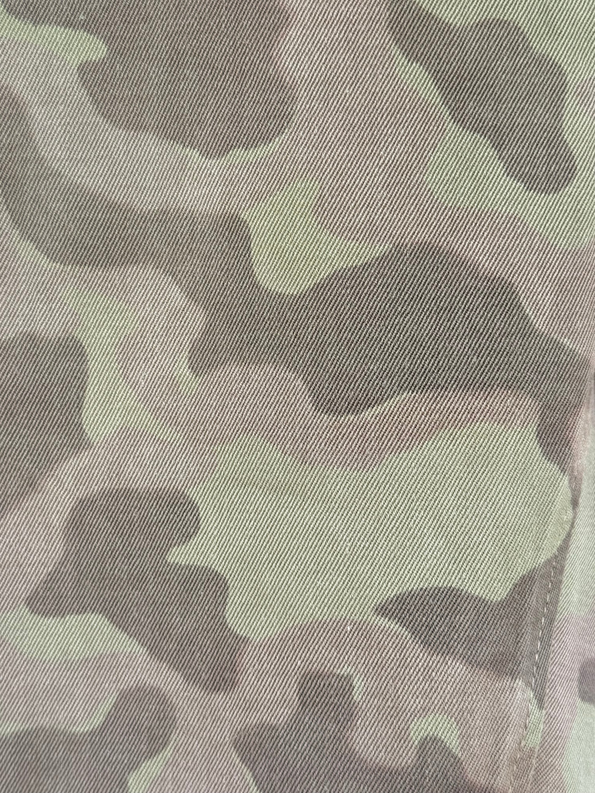 Close-up of a camouflage fabric pattern with shades of olive green, gray, and dark charcoal, showing a fine woven texture.