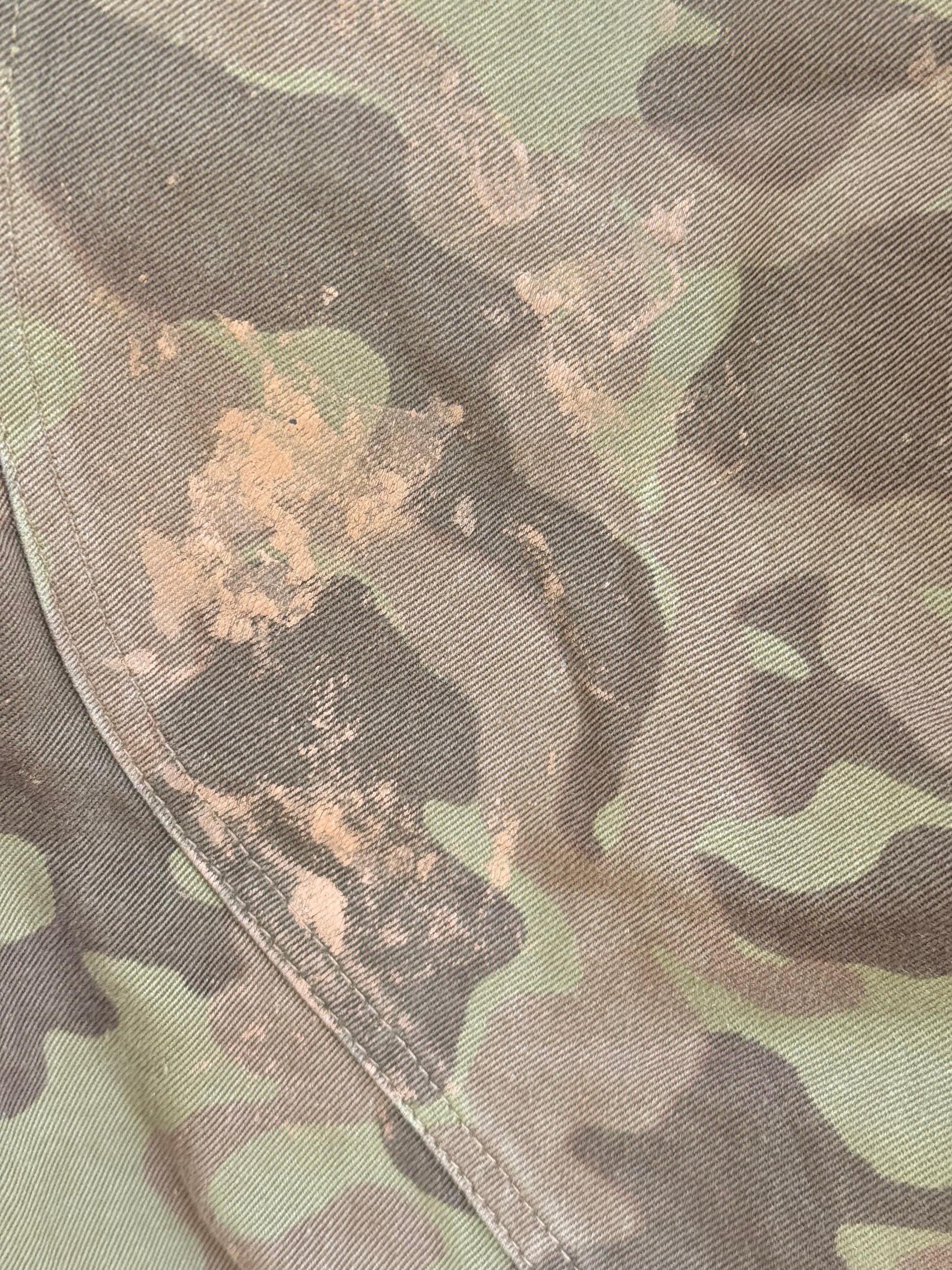 Close-up of camouflage fabric with a diagonal seam, showing a mix of green, brown, and tan tones.