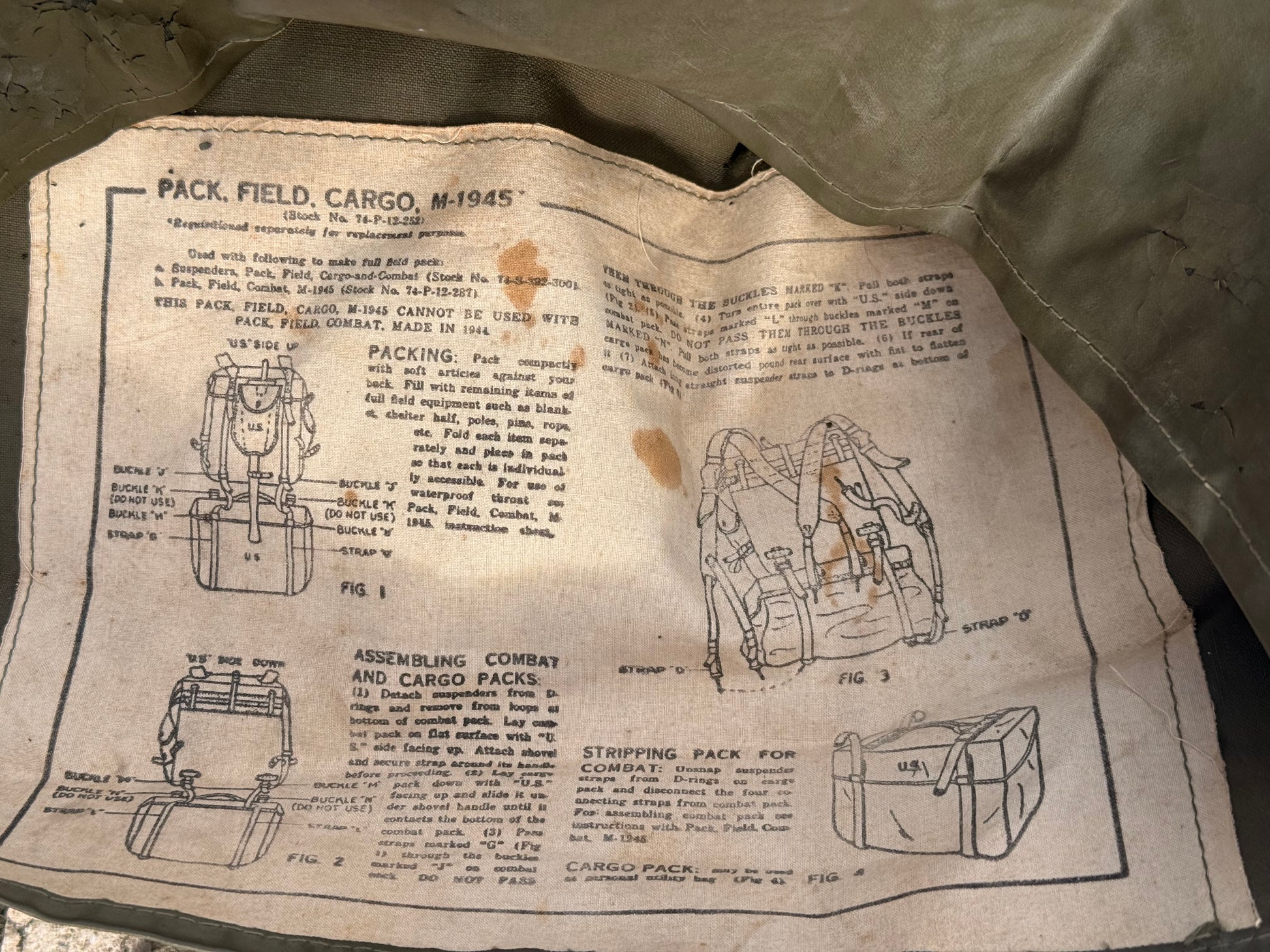 A vintage printed instruction sheet for a WWII-era military cargo pack, showing diagrams of packing, assembling, and stripping the pack, laid on top of olive drab canvas.