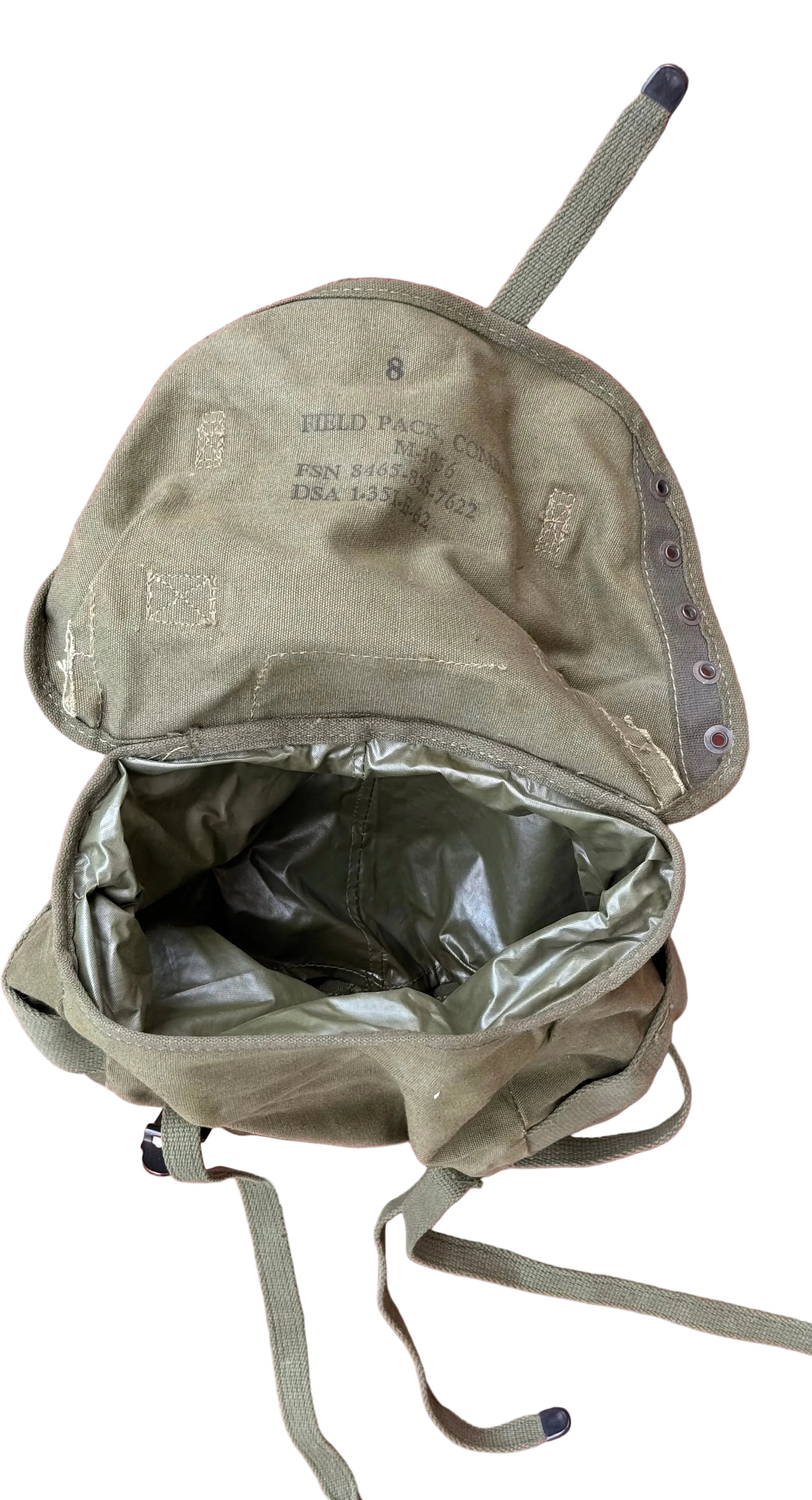An olive drab military-style canvas backpack shown open, revealing a dark interior lining, laid flat on a pink textured surface.
