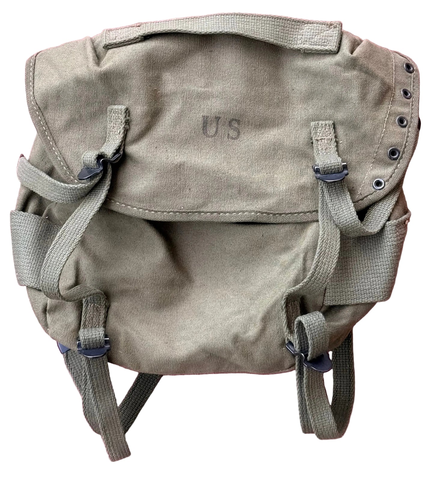 A vintage-style canvas utility backpack in a muted olive-tan color, featuring a top flap with 'U.S' embroidered on it, adjustable straps, and metal grommets, laid flat against a textured pink background.