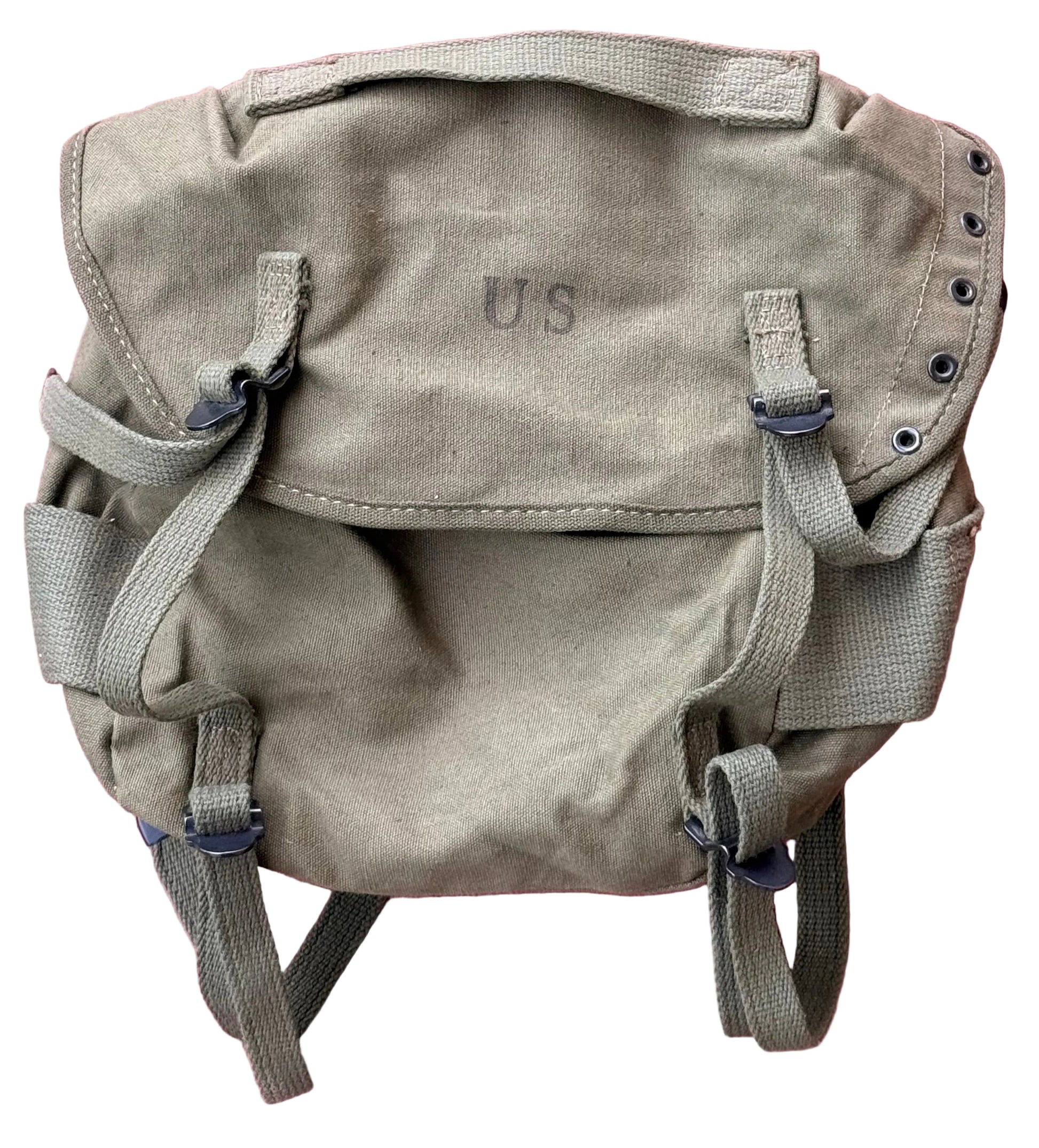 A vintage-style canvas utility backpack in a muted olive-tan color, featuring a top flap with 'U.S' embroidered on it, adjustable straps, and metal grommets, laid flat against a textured pink background.
