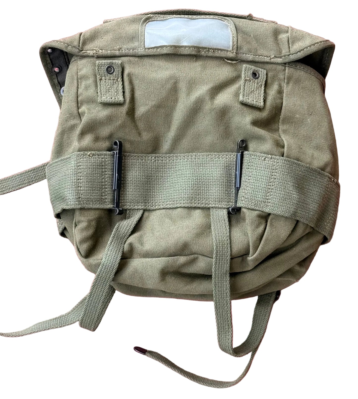An olive green military-style canvas backpack with a top flap, front webbing straps, and metal clips, shown against a textured pink background.