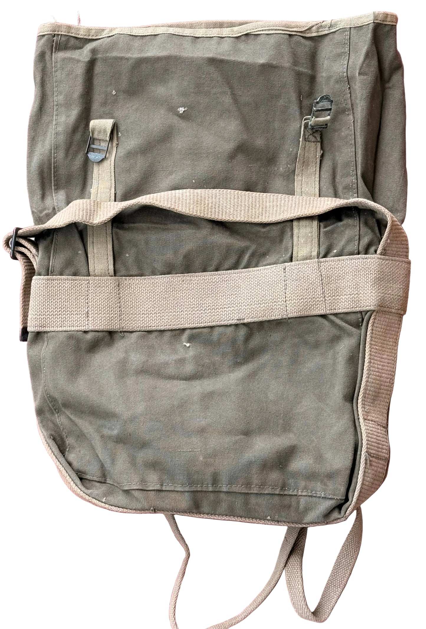 A vintage olive green canvas military-style backpack with beige webbing straps, laid flat on a textured pink surface.
