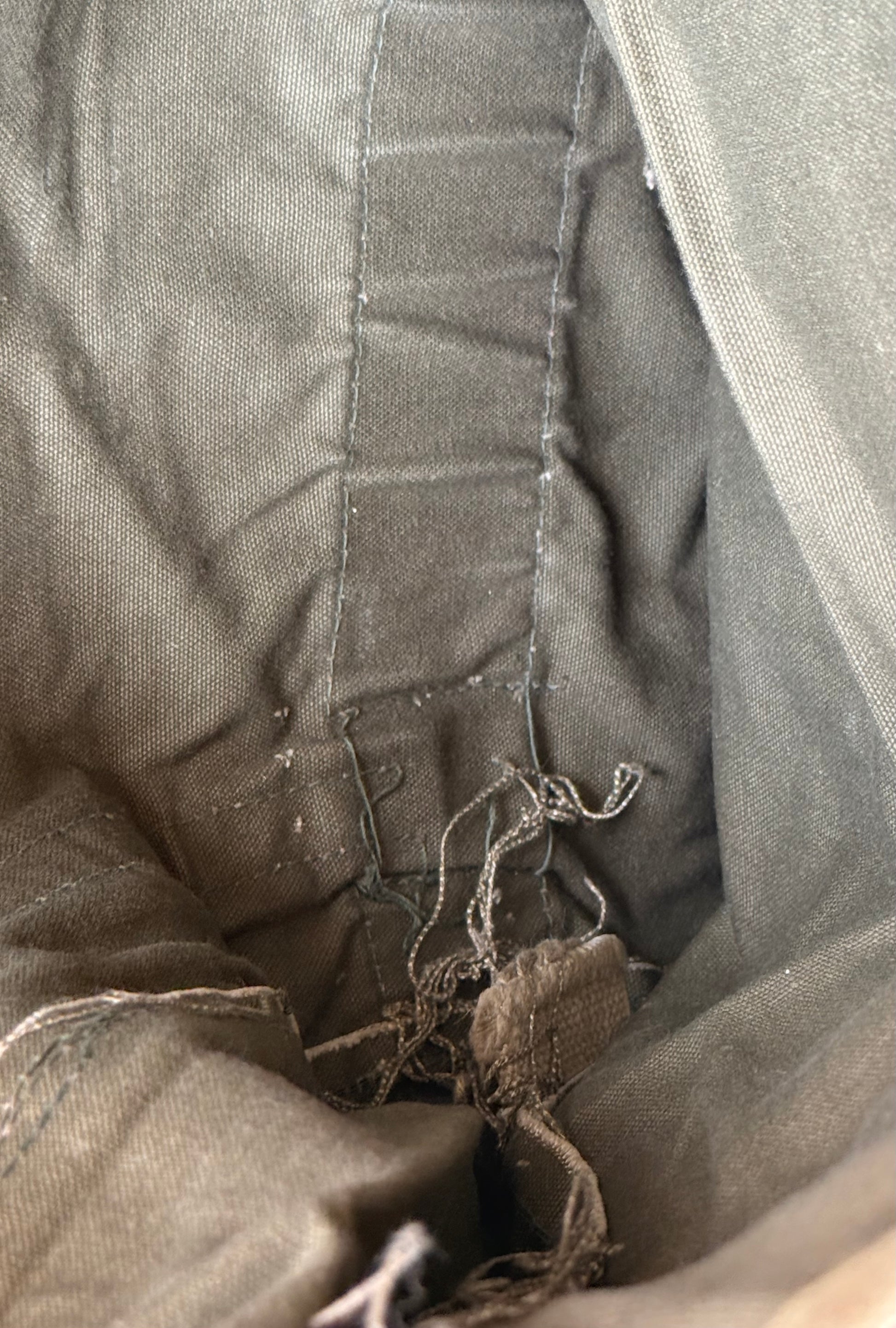 Close-up of the interior lining of a gray fabric bag or pouch, showing stitched seams and frayed drawstring threads near the opening.