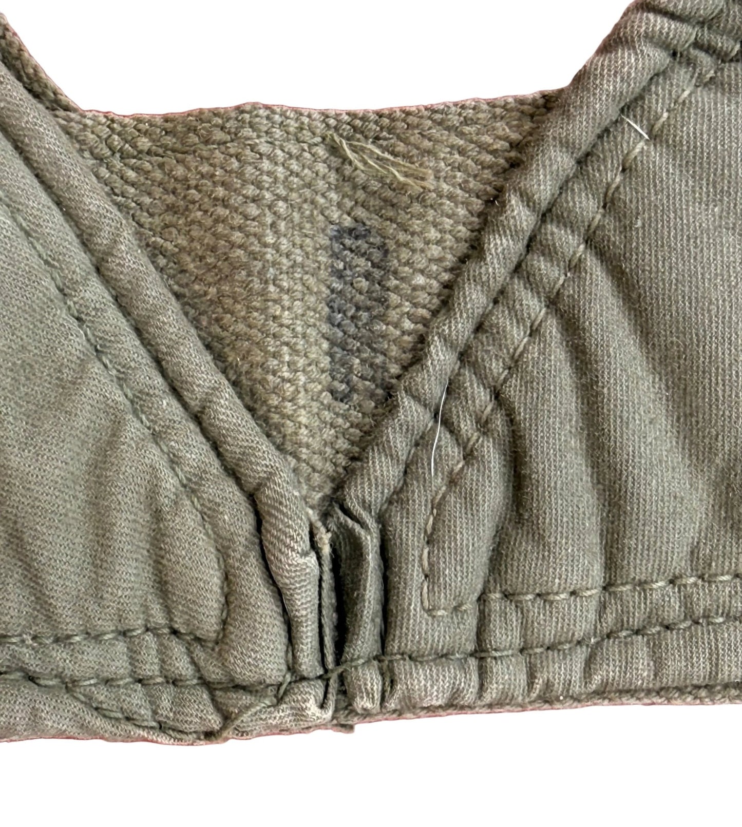 Close-up of an olive green bra cup and center gore area, showing the fabric texture, stitching, and a small interior label, placed on a pink textured background.