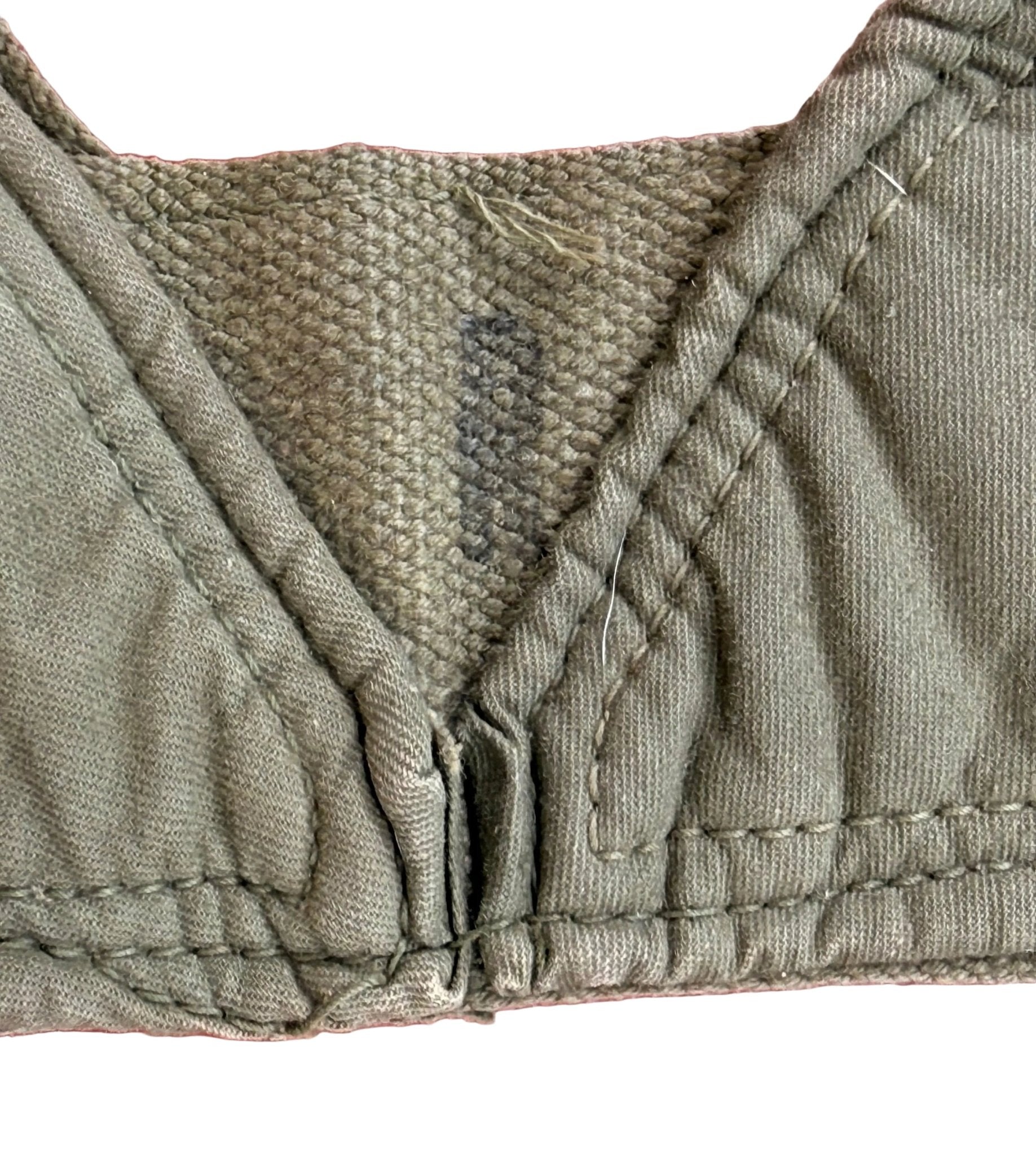 Close-up of an olive green bra cup and center gore area, showing the fabric texture, stitching, and a small interior label, placed on a pink textured background.