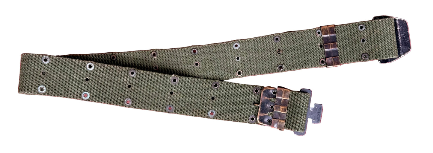 An olive green canvas utility belt with metal rivets and a camouflage-patterned buckle, laid flat on a textured red surface.