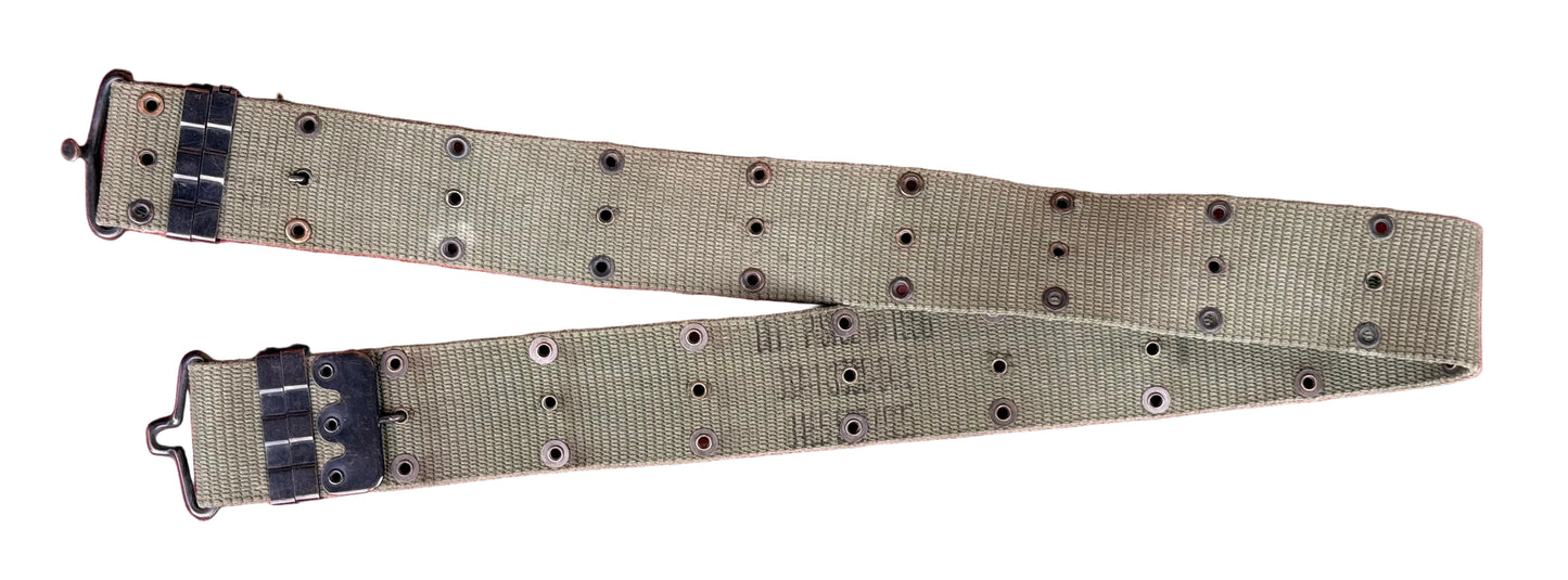 A khaki canvas watch strap with black metal hardware and adjustment loops, laid flat on a textured red surface.