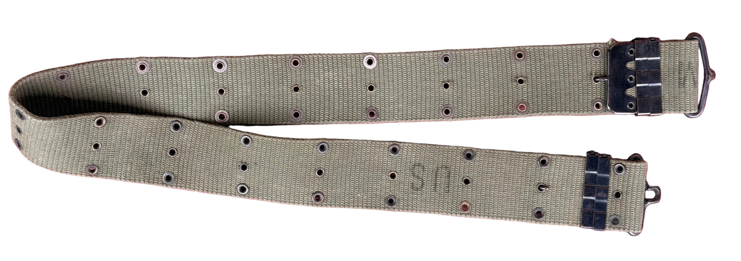An olive drab canvas military belt with metal eyelets and black plastic buckle components, laid flat on a textured red background.