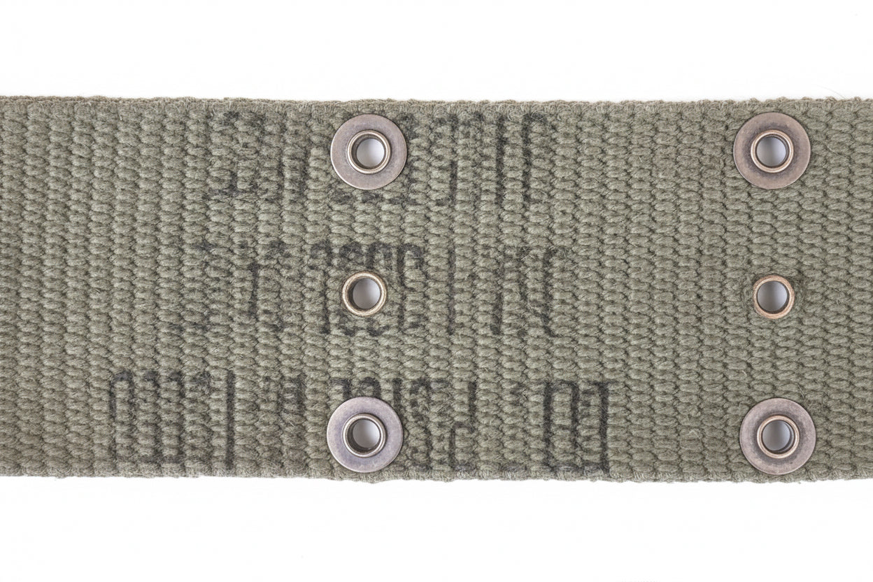 Close-up of a woven olive drab canvas strap with metal grommets, showing faint stamped text on the fabric against a pink background.