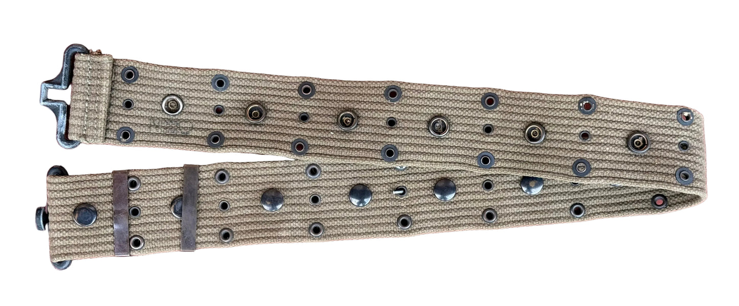 A tan canvas belt with black metal rivets and a black metal buckle, laid flat on a textured red surface.