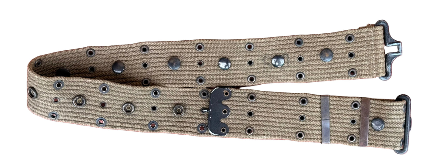 A tan canvas utility belt with silver-toned metal rivets and a black plastic buckle, laid flat on a textured reddish-pink surface.