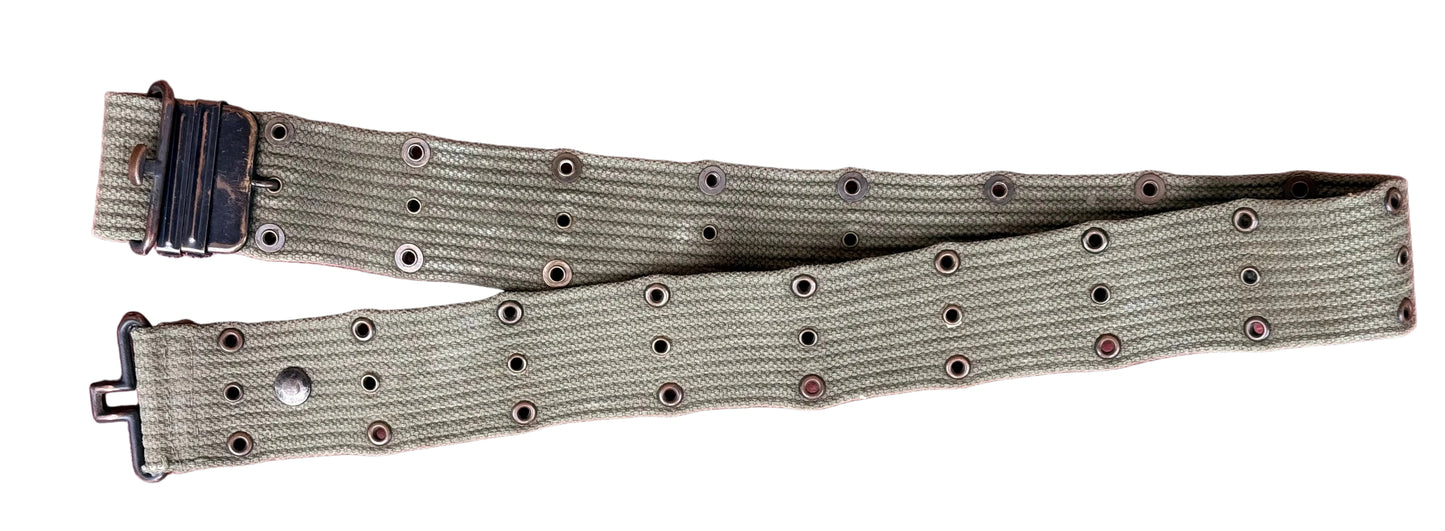 An olive green canvas watch strap with metal eyelets and a black plastic buckle, laid flat on a textured red surface.