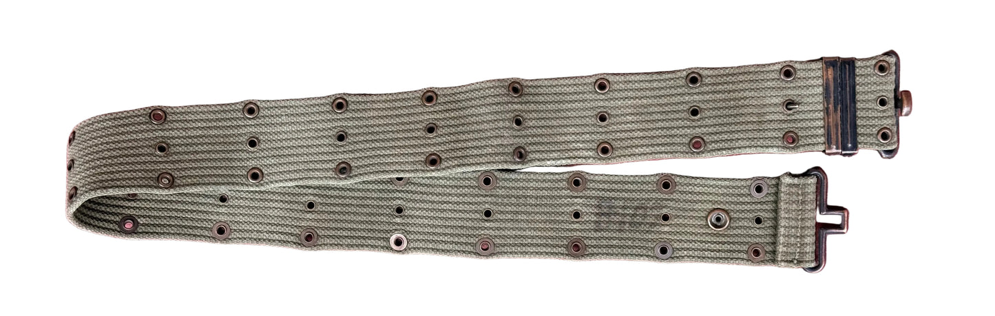 A vintage olive green canvas watch strap with metal grommets and a black buckle, laid flat on a textured pink background.