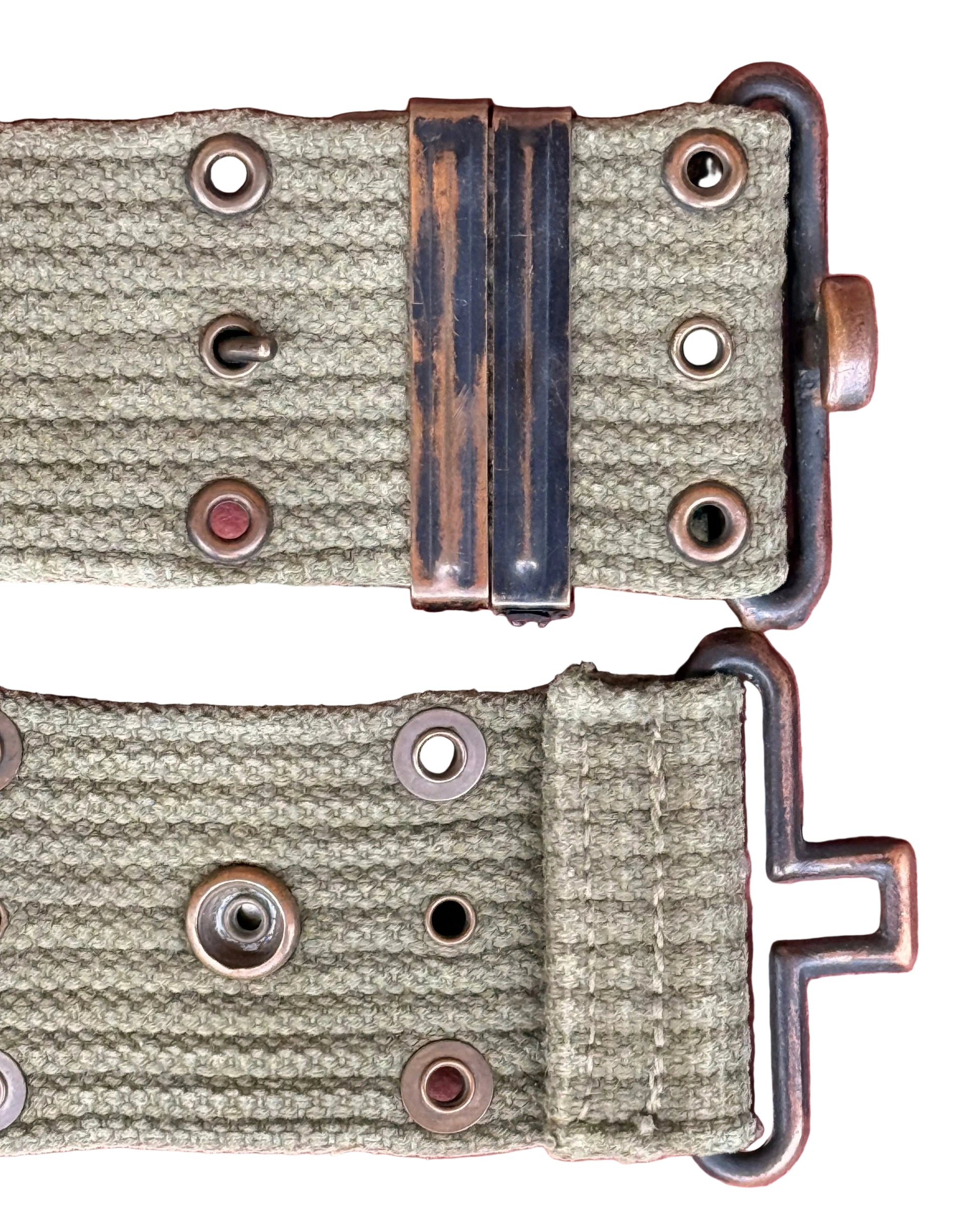 Close-up of a woven olive green watch strap with a dark metal buckle and brass-toned eyelets, laid flat on a pink textured background.