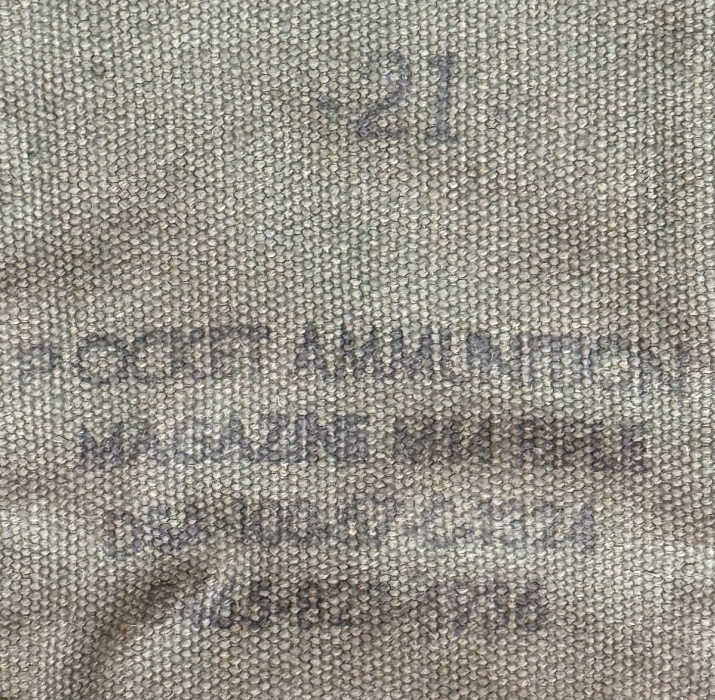 Close-up of a beige woven fabric with dark gray stamped text reading 'POCKET AMMUNITION MAGAZINE MEGA BIBLE' and a stamped number '21'.