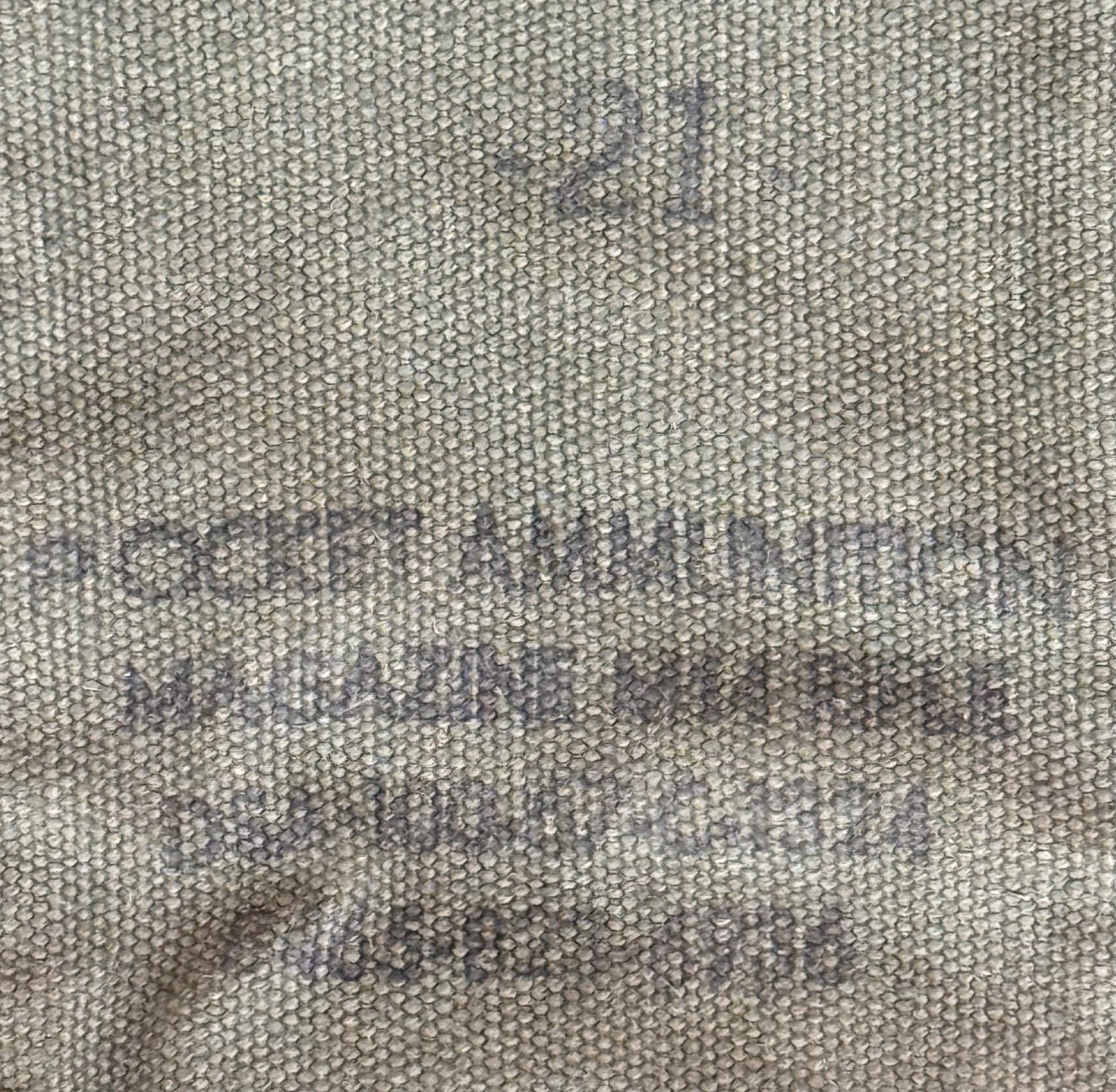 Close-up of a beige woven fabric with dark gray stamped text reading 'POCKET AMMUNITION MAGAZINE MEGA BIBLE' and a stamped number '21'.
