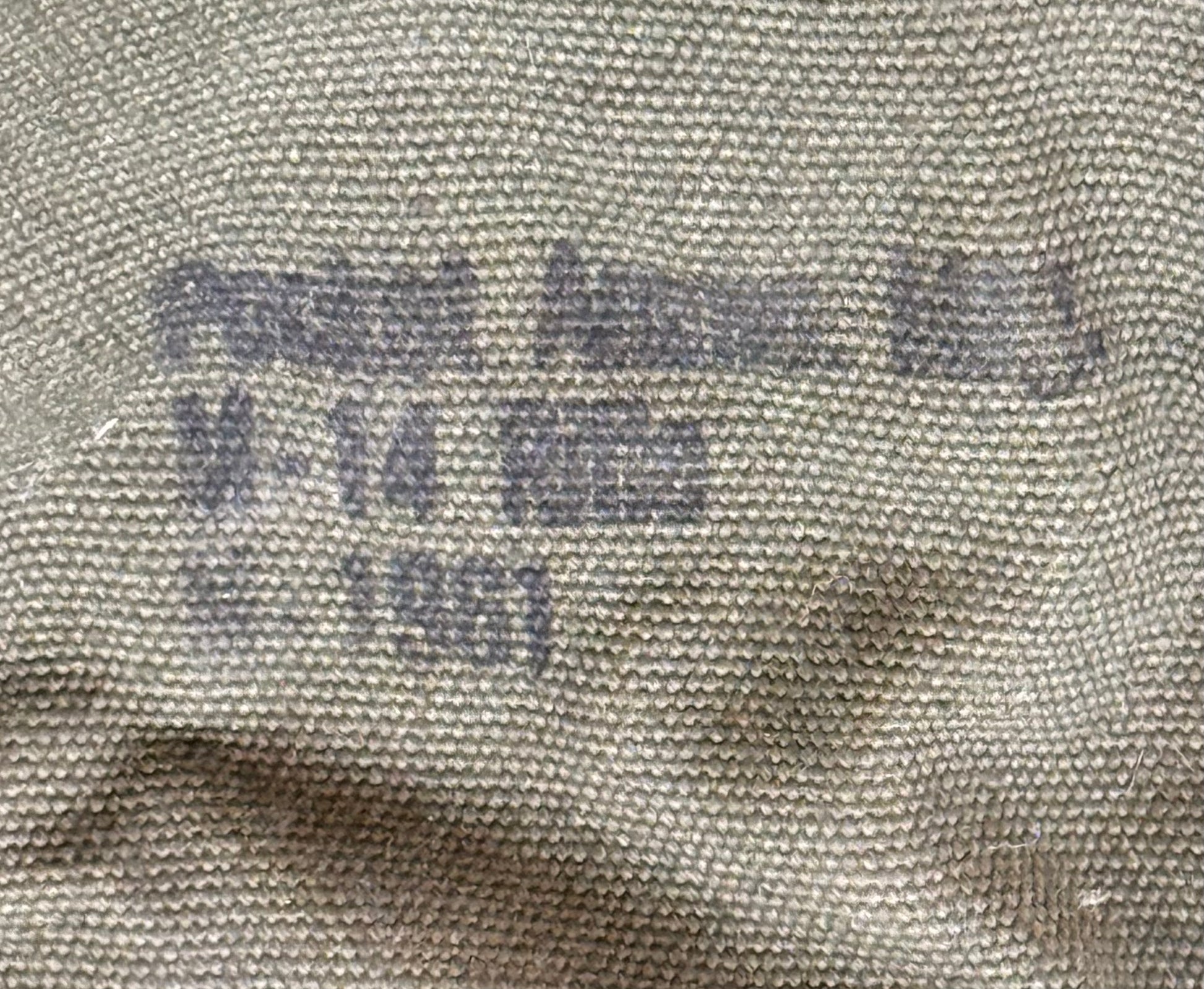Close-up of a beige woven fabric surface with faded dark printed text reading 'Pocatello Army Mill', 'M-14 600', and 'No. 1961'.