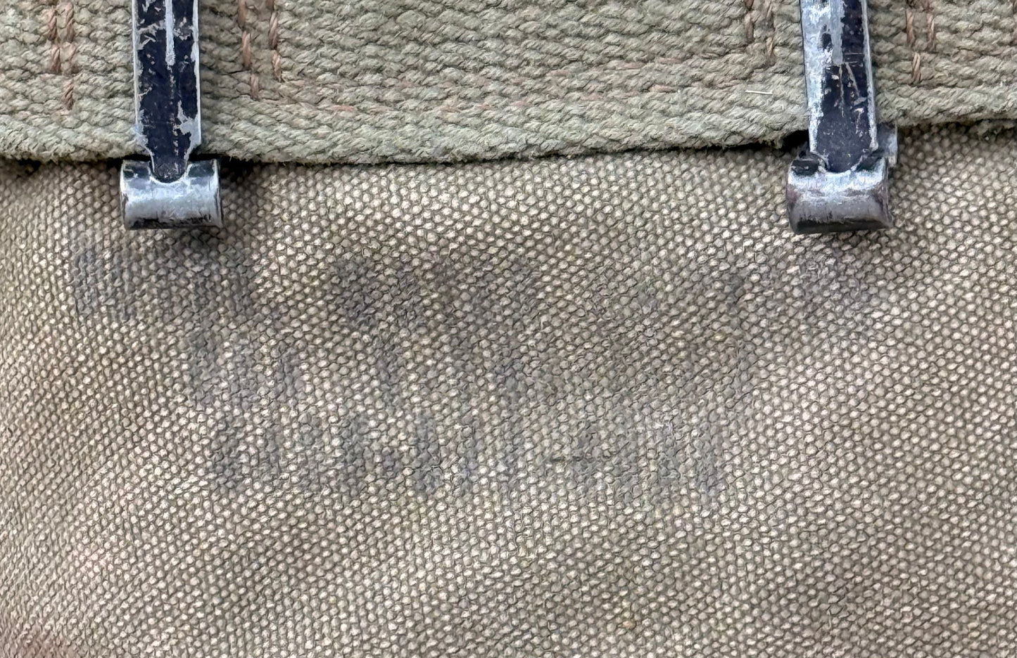 Close-up of a canvas bag or backpack showing the woven fabric texture, a tan top strap, and two silver metal zipper pulls with worn white paint.