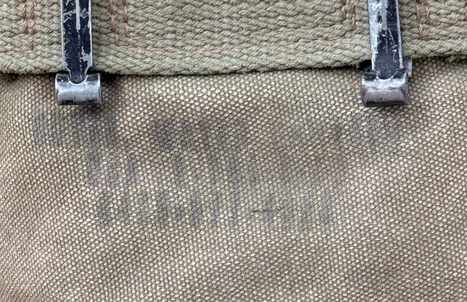 Close-up of a canvas bag or backpack showing the woven fabric texture, a tan top strap, and two silver metal zipper pulls with worn white paint.
