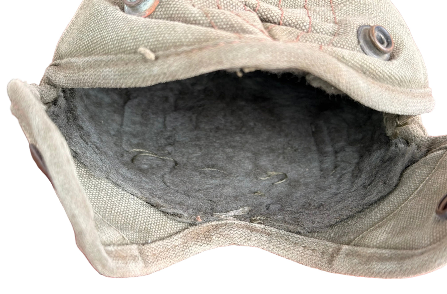 A close-up of a vintage canvas utility pouch with a dark gray felt lining, resting on a red textured surface.
