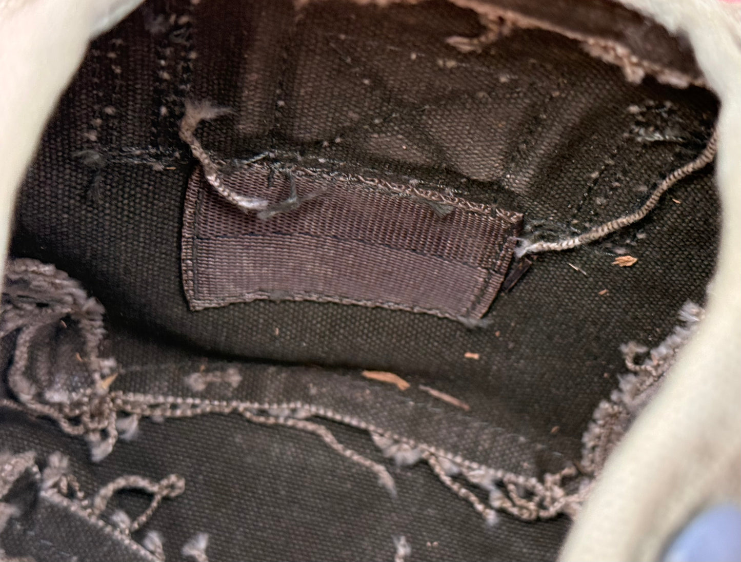 Close-up of the interior lining of a dark brown canvas shoe or bag, showing a sewn-on brand label and frayed, distressed edges.