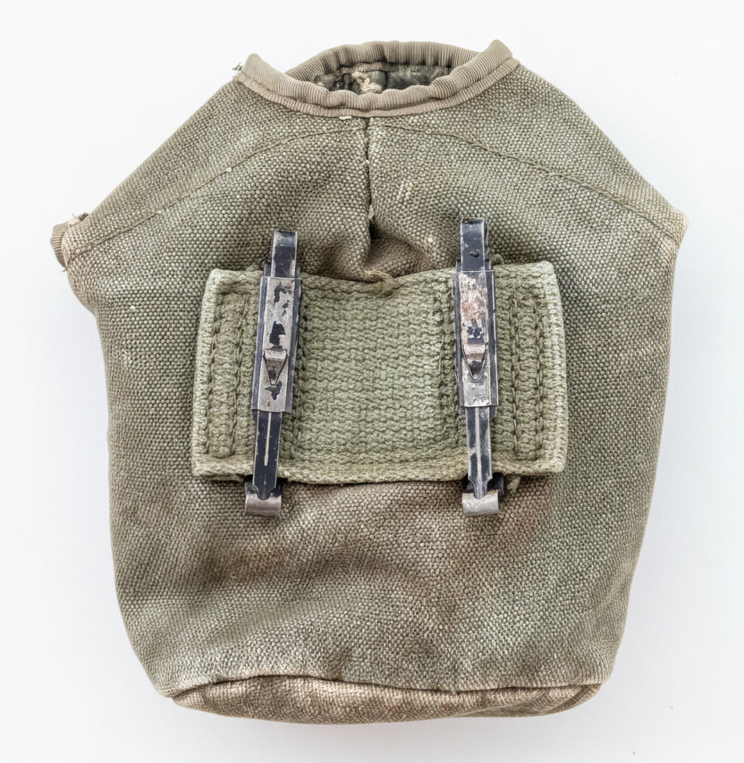 A vintage olive green canvas utility pouch with a front pocket and two black plastic clips, displayed against a textured red background.