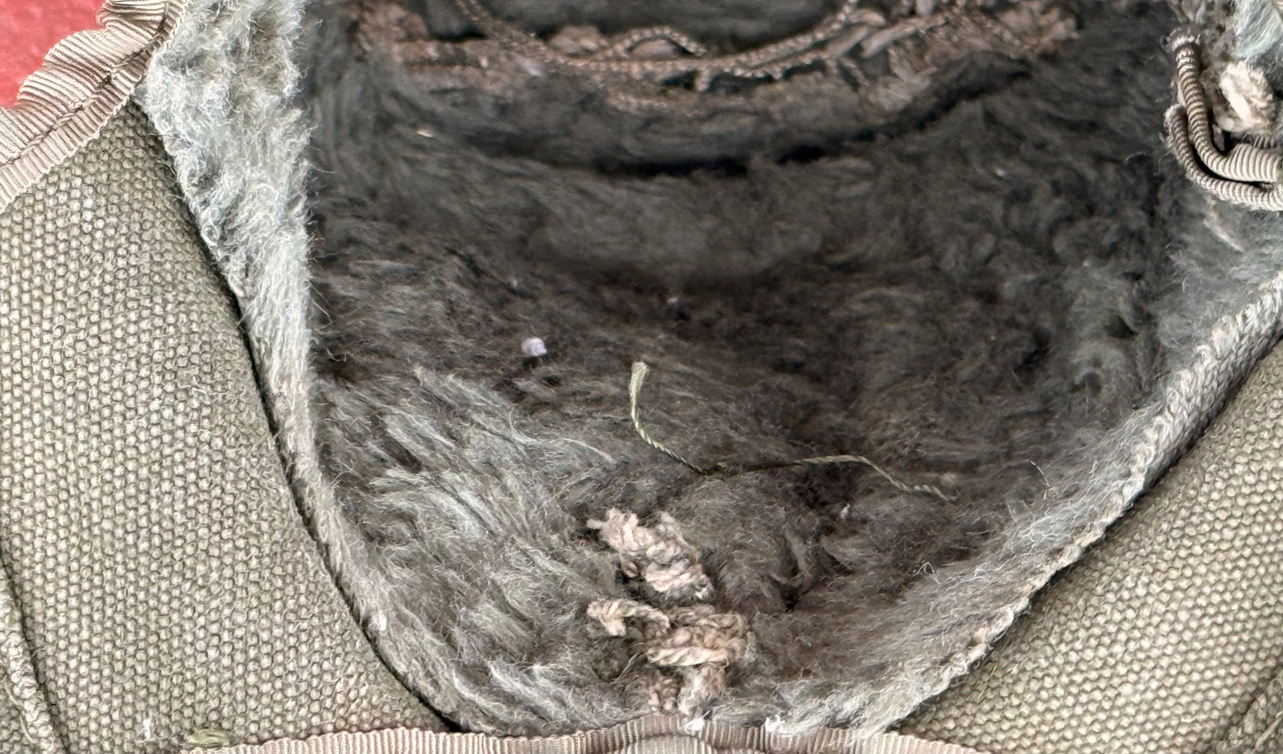 Close-up of the interior lining of a bag or pouch, showing a dark gray and brown fur or wool-like lining attached to a beige woven fabric exterior.