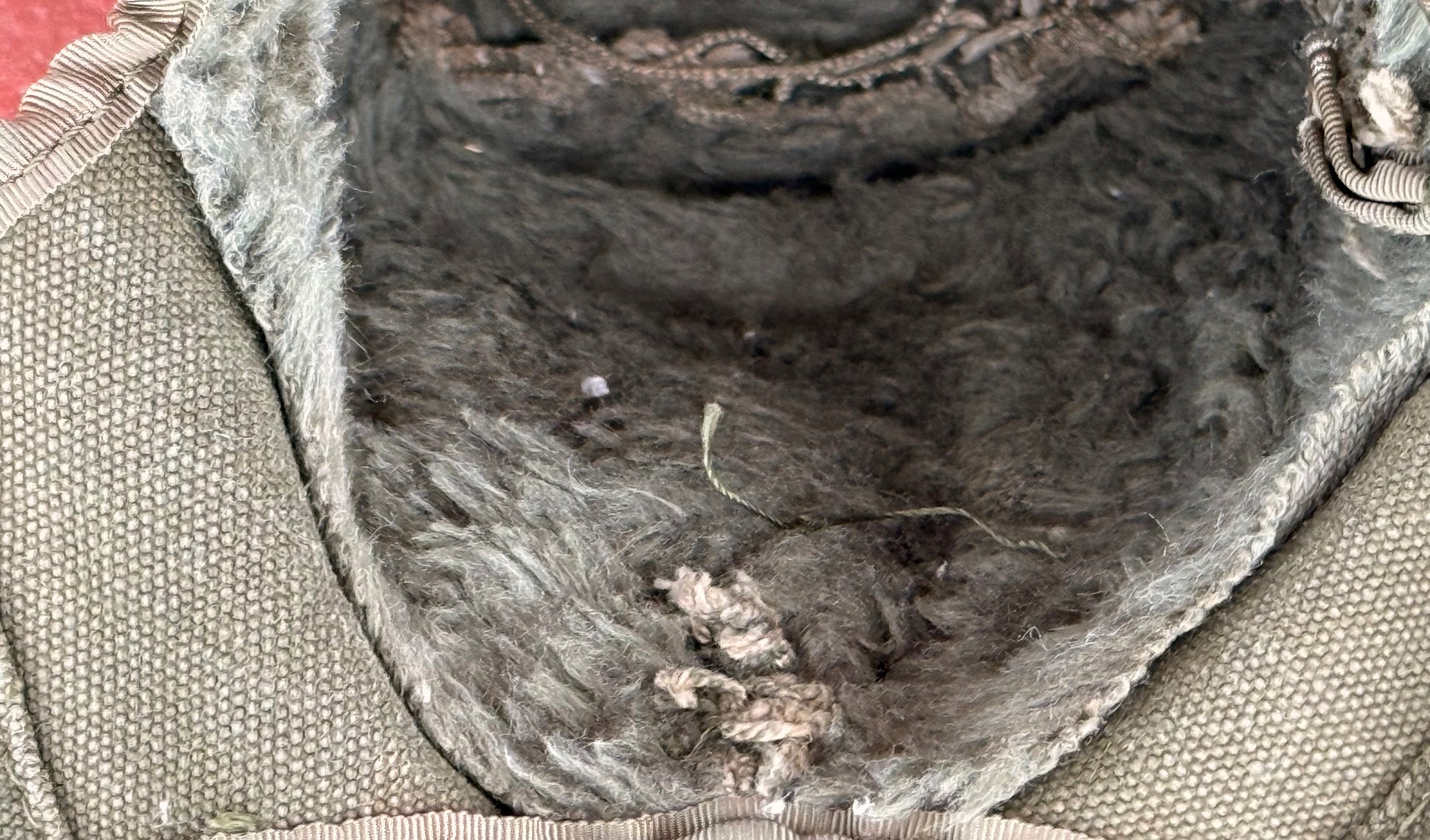 Close-up of the interior lining of a bag or pouch, showing a dark gray and brown fur or wool-like lining attached to a beige woven fabric exterior.