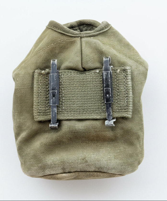 An olive drab canvas pouch with two metal clips on a red textured background.