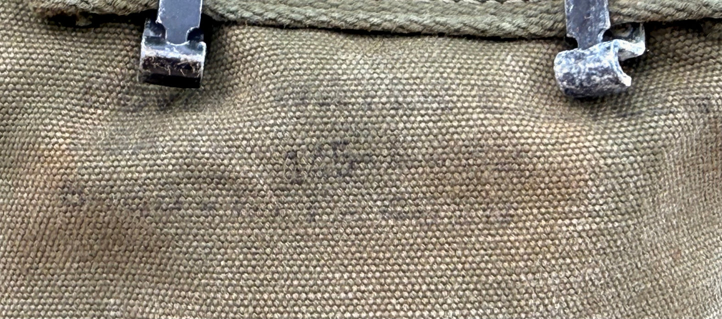 Close-up of a canvas bag or pouch in a muted tan/khaki fabric, showing the woven texture and two dark metal clips at the top.