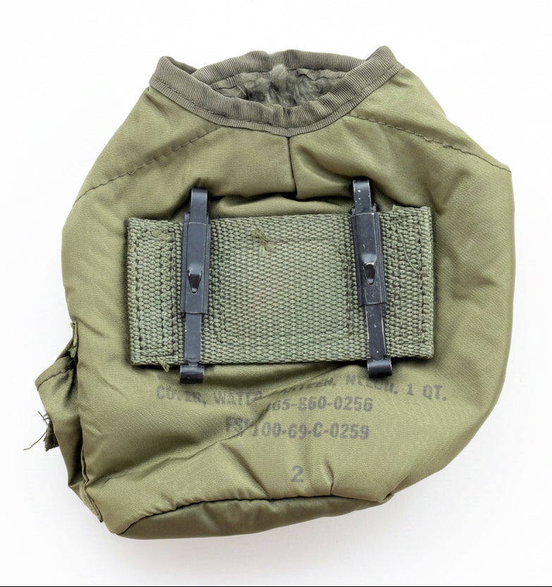 An olive green military-style water bottle pouch with black plastic buckle straps and a central webbing patch, laid flat on a textured red surface.