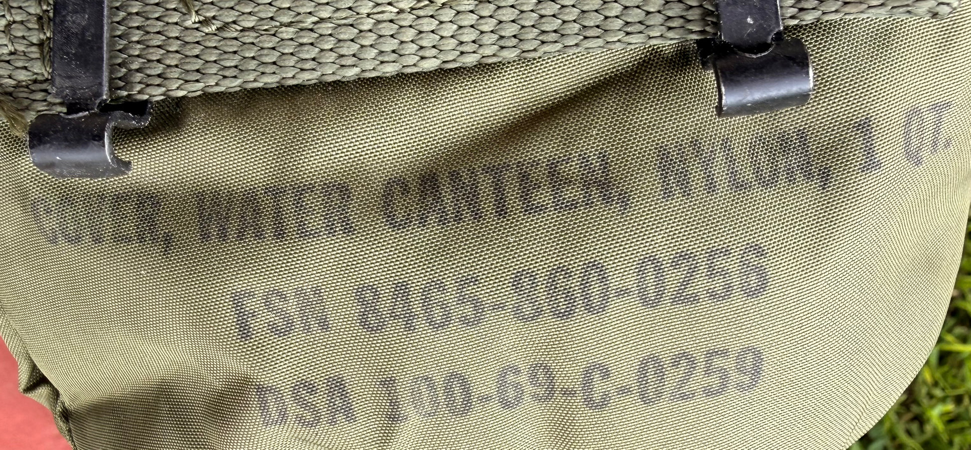 Close-up of an olive green nylon water canister cover with black printed text and black plastic clips attached.