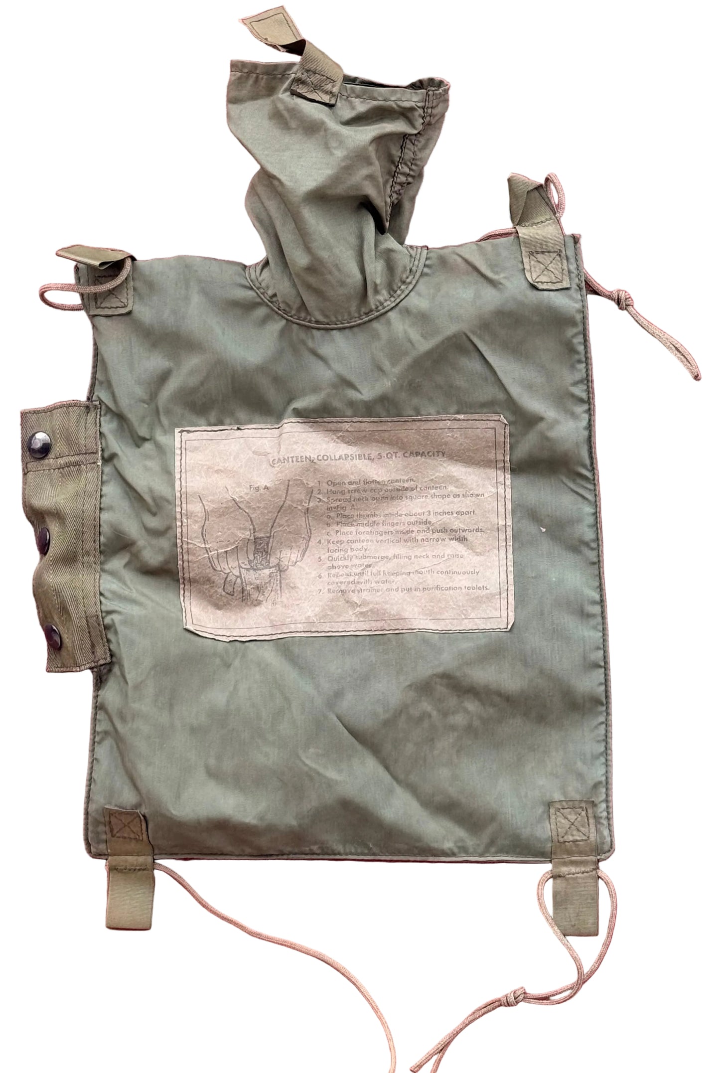 An olive green military-style canvas pouch with a hood, shown laid flat against a textured pink background. The pouch features a large rectangular patch with printed text and a sketch, along with drawstring ties and metal snap closures.