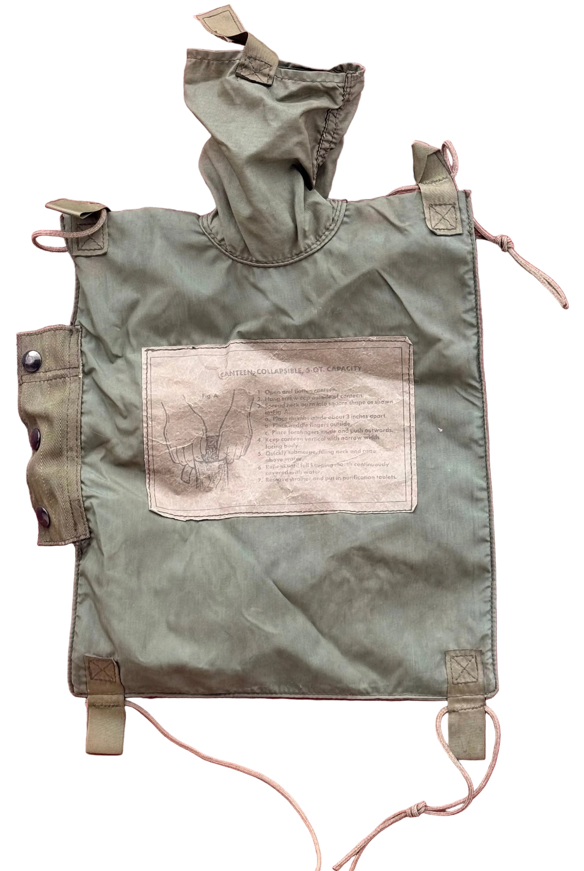 An olive green military-style canvas pouch with a hood, shown laid flat against a textured pink background. The pouch features a large rectangular patch with printed text and a sketch, along with drawstring ties and metal snap closures.