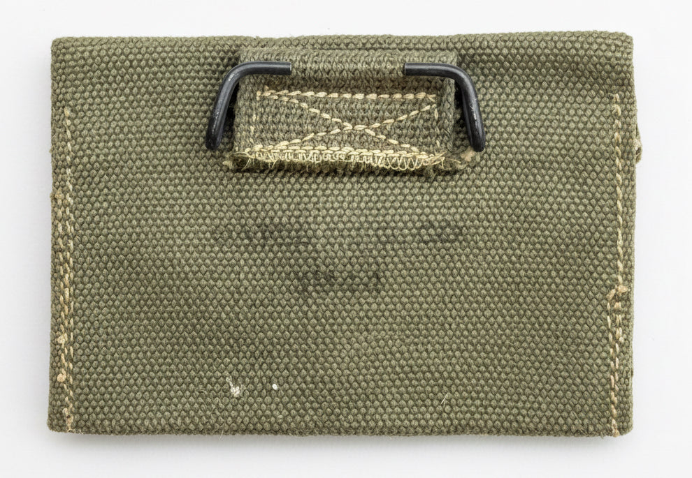 An olive green canvas utility pouch with a black plastic loop and a stitched label area, shown on a textured red background.