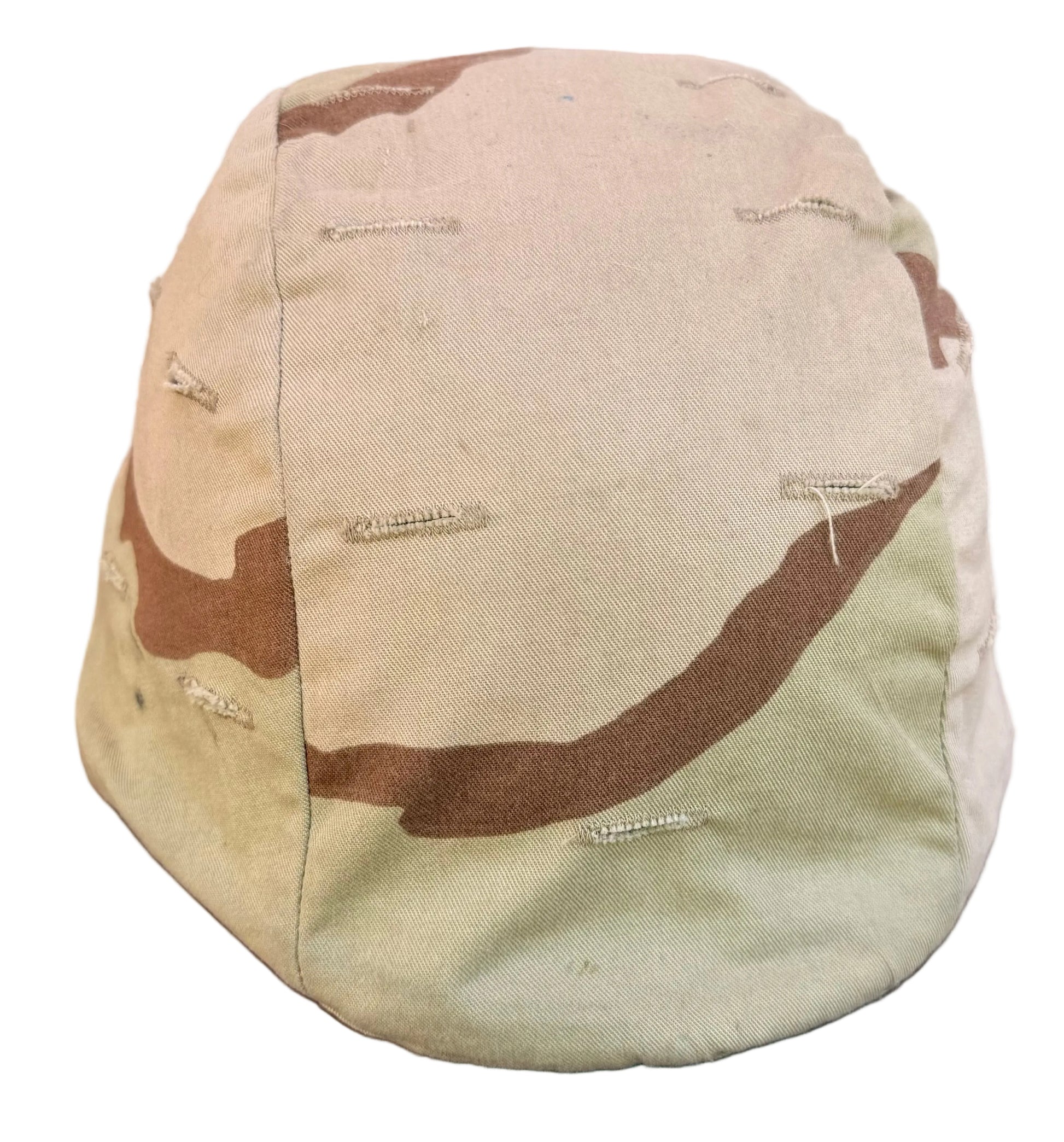 A vintage camouflage baseball cap in a desert camo pattern, resting on a reddish-brown wooden surface with a brick wall and a white sneaker blurred in the background.