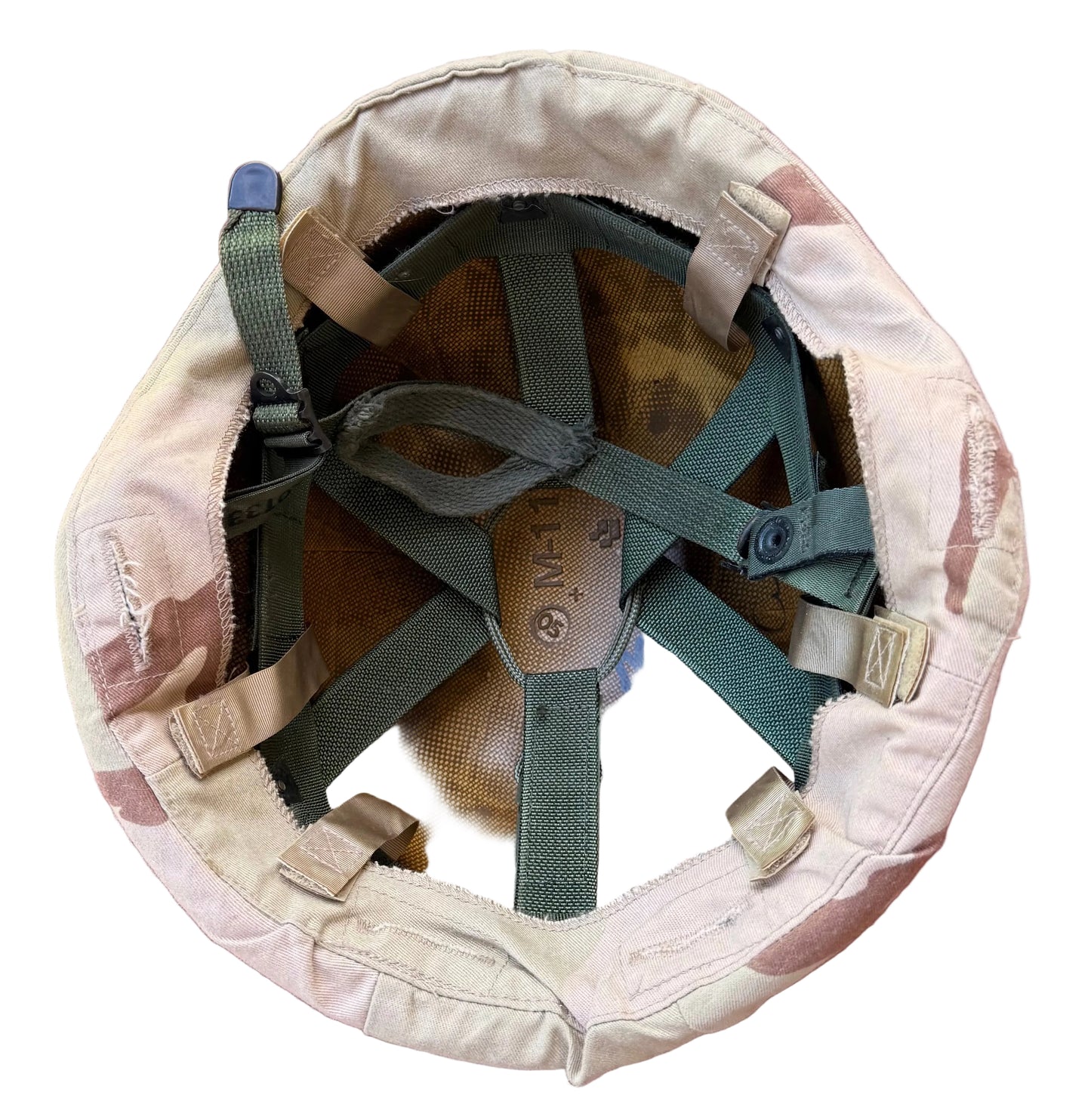 Top-down view of a military combat helmet interior showing a desert camouflage fabric outer shell, tan mesh padding, and green adjustable chin straps on a dusty rose background.