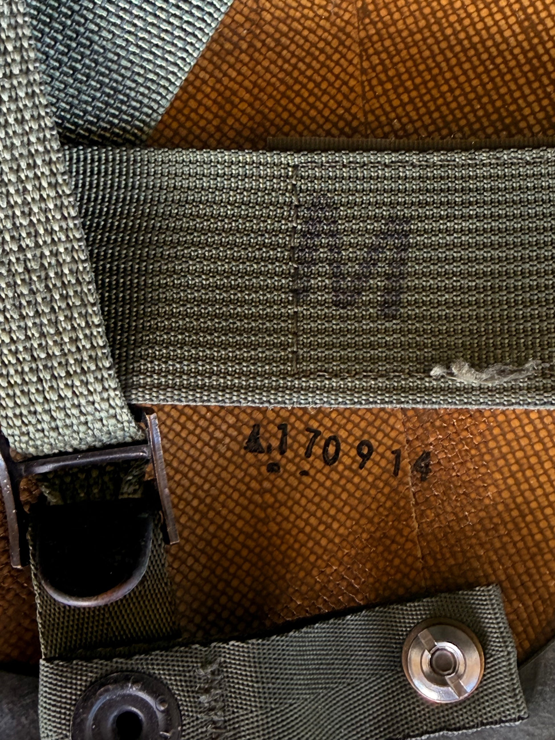 Close-up of a vintage olive green webbed strap and canvas panel with stamped serial numbers '4170914' and faded lettering.