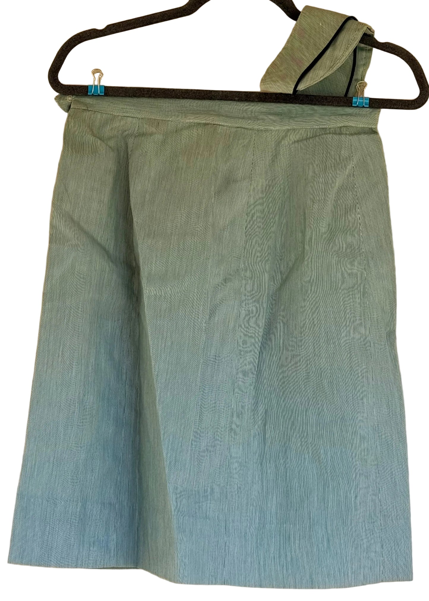 A light blue-green textured skirt hanging on a black hanger against a beige wall.