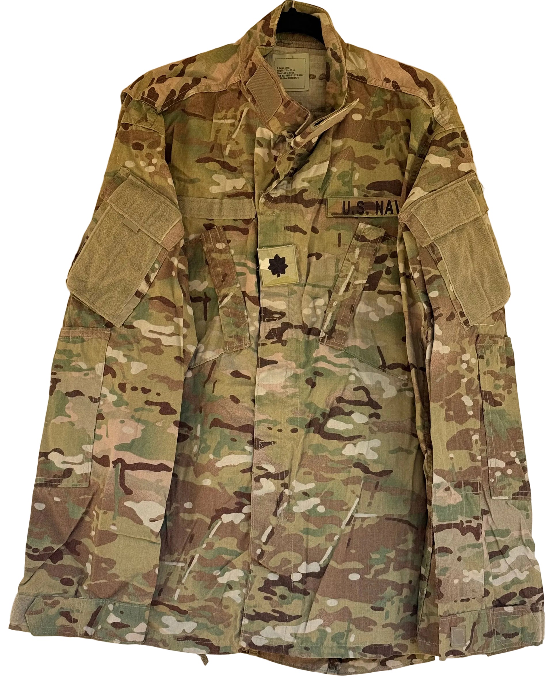 A U.S. Navy combat utility jacket in MultiCam camouflage pattern, hanging on a black hanger against a beige wall.