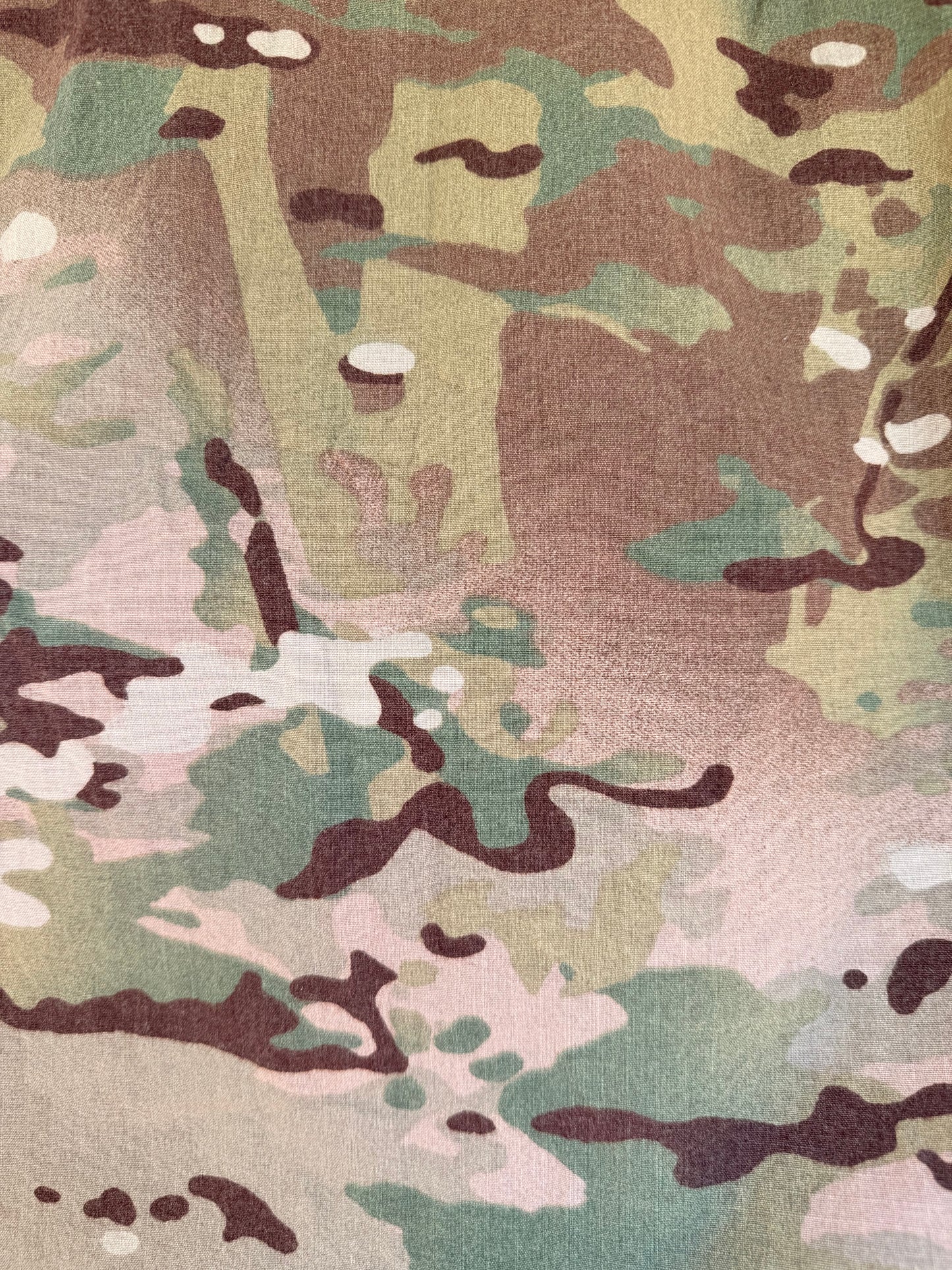 A close-up of a camouflage pattern with blended shades of olive green, tan, brown, beige, and light pink, showing a fabric-like texture.