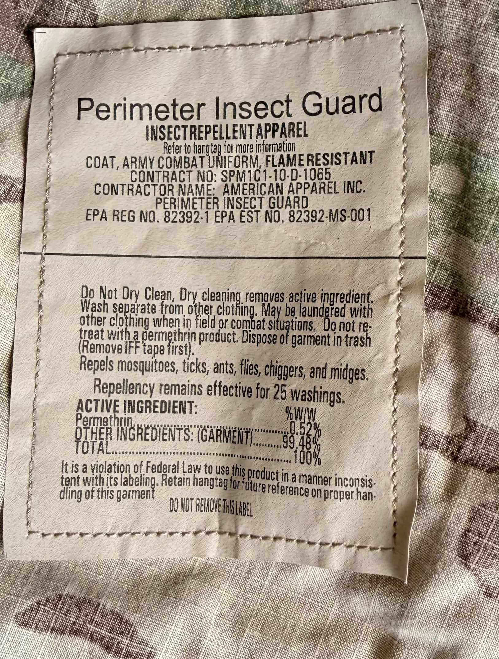 A close-up of a sewn fabric product label reading 'Perimeter Insect Guard' with product details and ingredients, placed on a textured beige and brown fabric background.